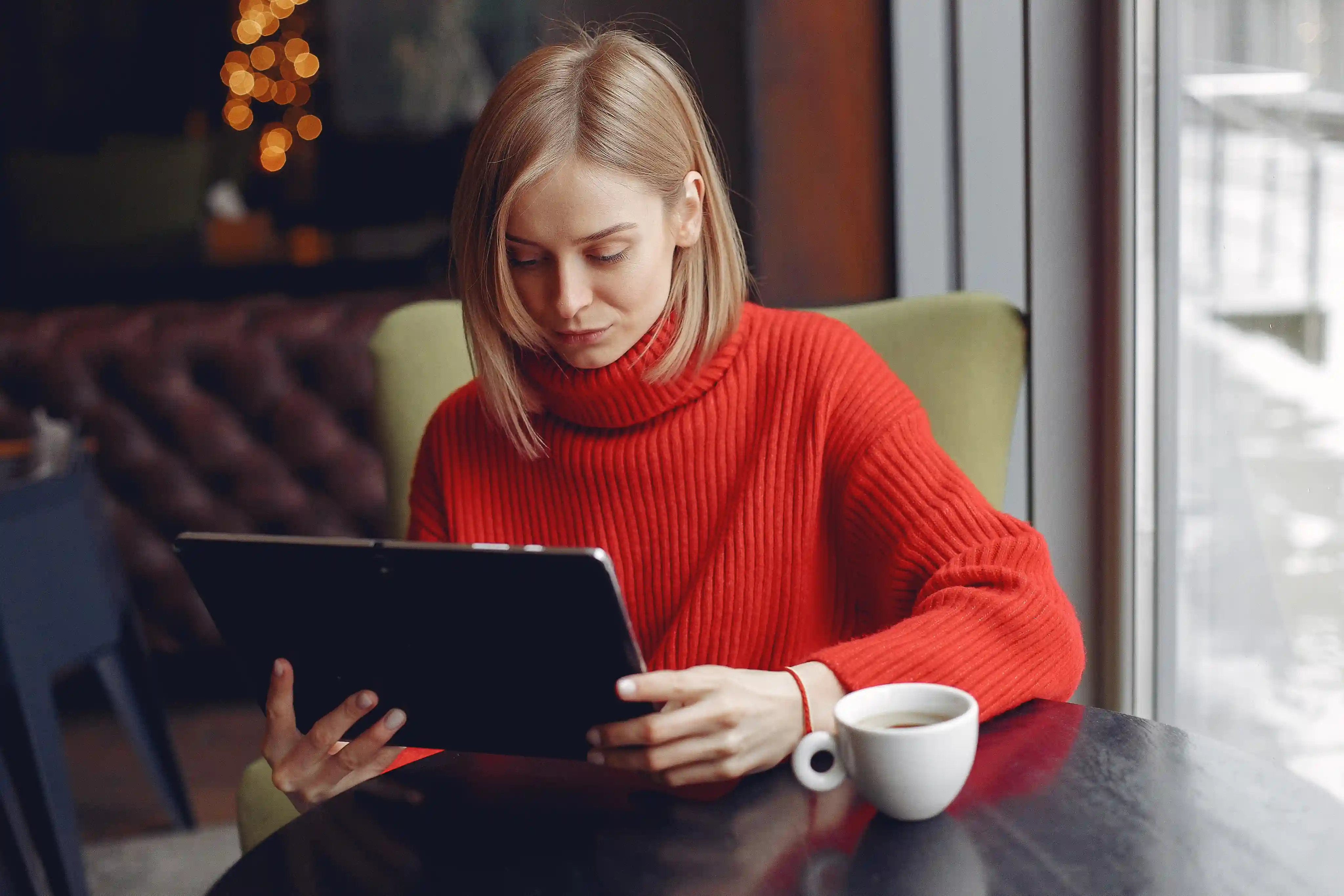 Woman in a red sweater browsing a tablet, likely looking for Deriv news or press releases