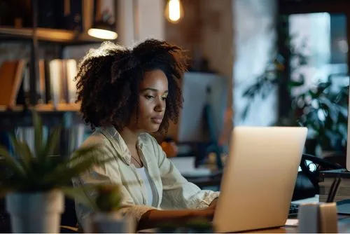 Woman on laptop browsing Deriv Partner Help Centre for guidance on the affiliate program.