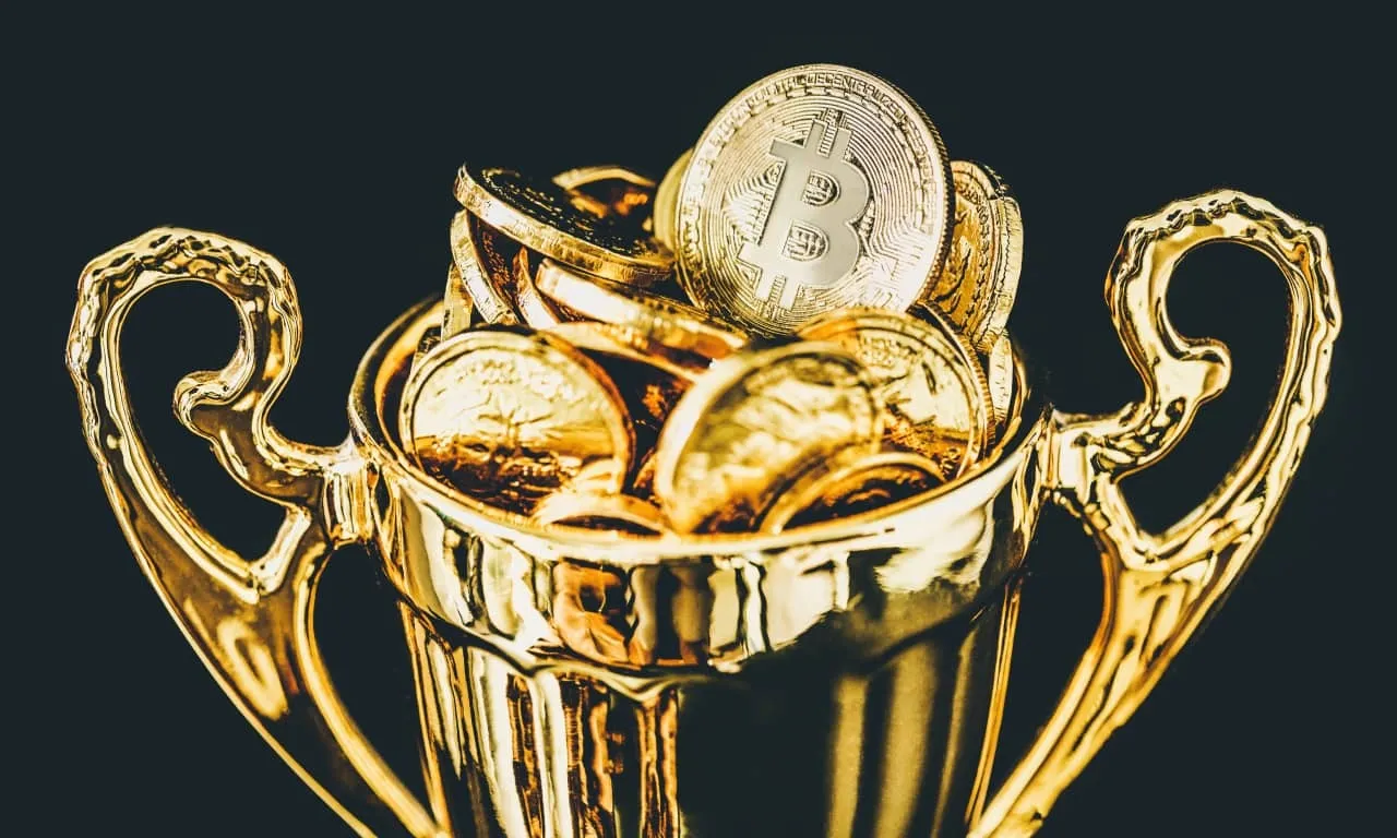 Un trofeo dorado lleno de brillantes monedas de oro, con una prominente moneda símbolo de Bitcoin encima.