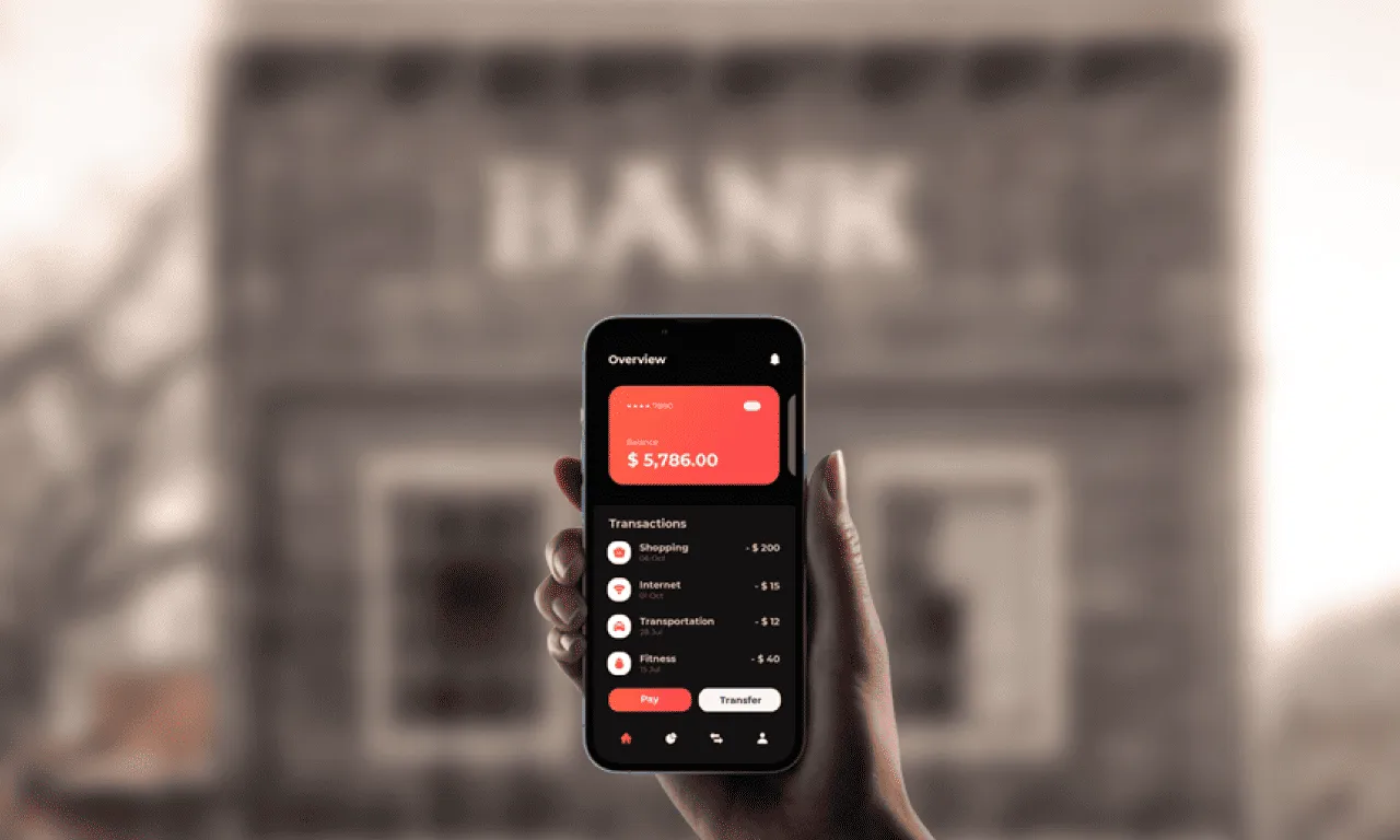 A hand holds a smartphone displaying a finance app, with a blurred traditional bank building backdrop.