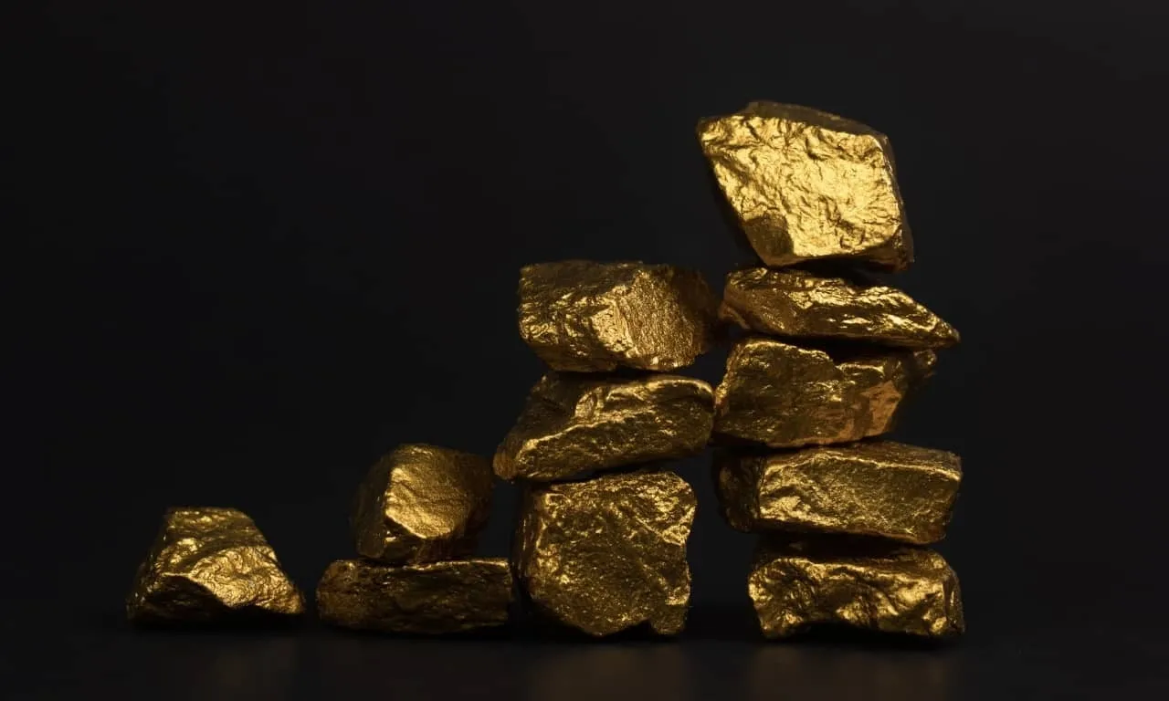 Un montón de brillantes pepitas de oro sobre un fondo negro, representando al oro como un valioso commodity de trading en Deriv.