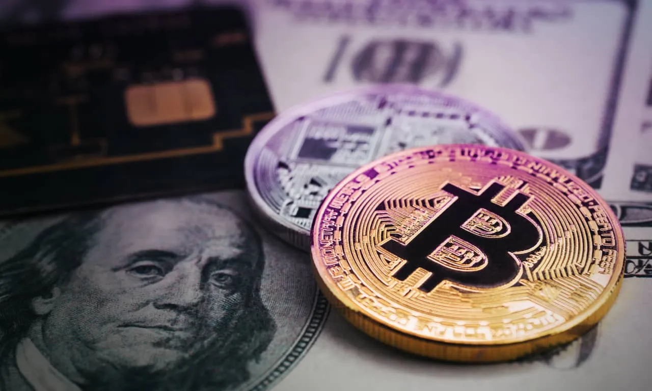 Close-up of a golden Bitcoin coin, a silver cryptocurrency coin, a circuit board, and a U.S. dollar bill.