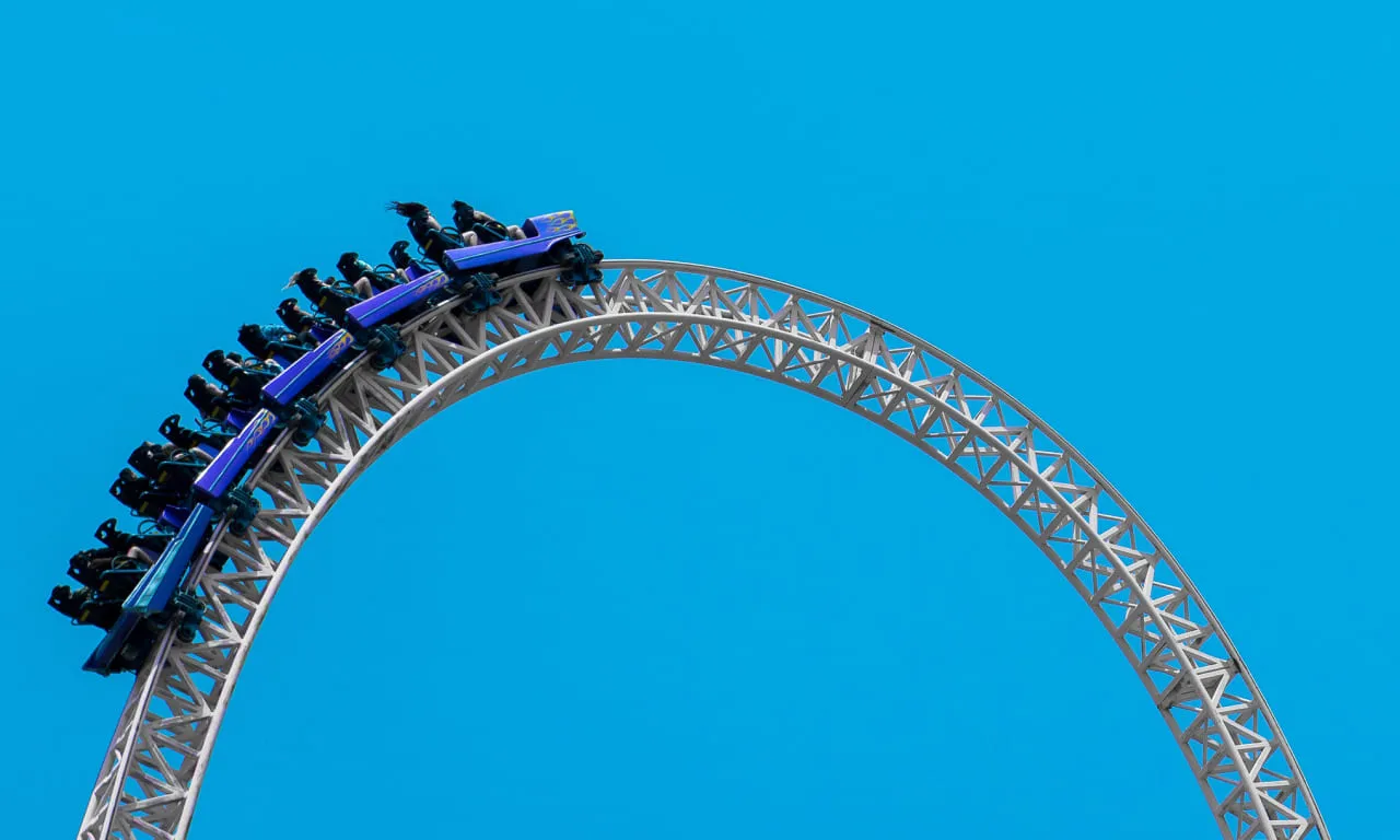 Una montagna russa che sale lungo una ripida curva sotto un cielo blu chiaro, simboleggiando gli alti e bassi del mercato.