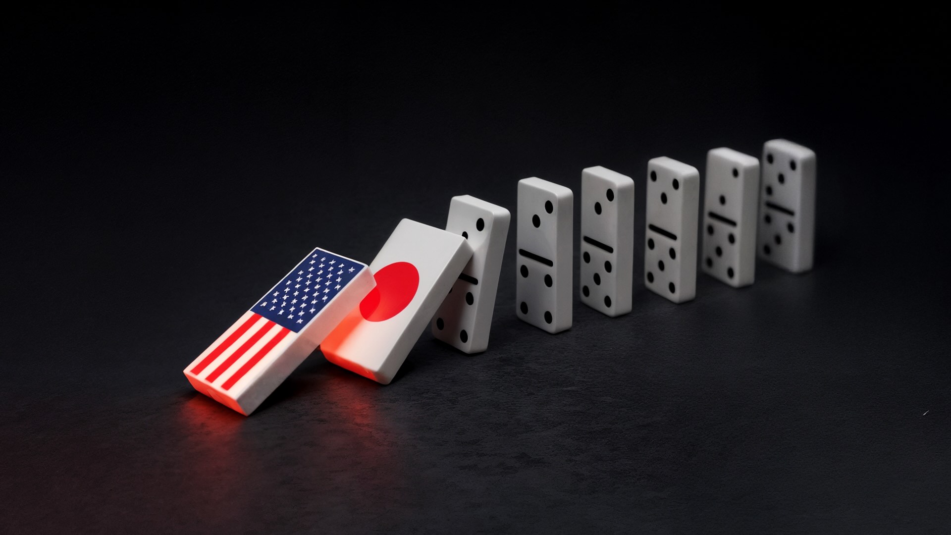 一排多米诺骨牌，最前端的两块分别是美国和日本的国旗，美国的多米诺骨牌倒下，推动了日本的多米诺骨牌，象征着金融传染。 美国的多米诺骨牌正在倾倒，推动日本的多米诺骨牌，象征金融传染。